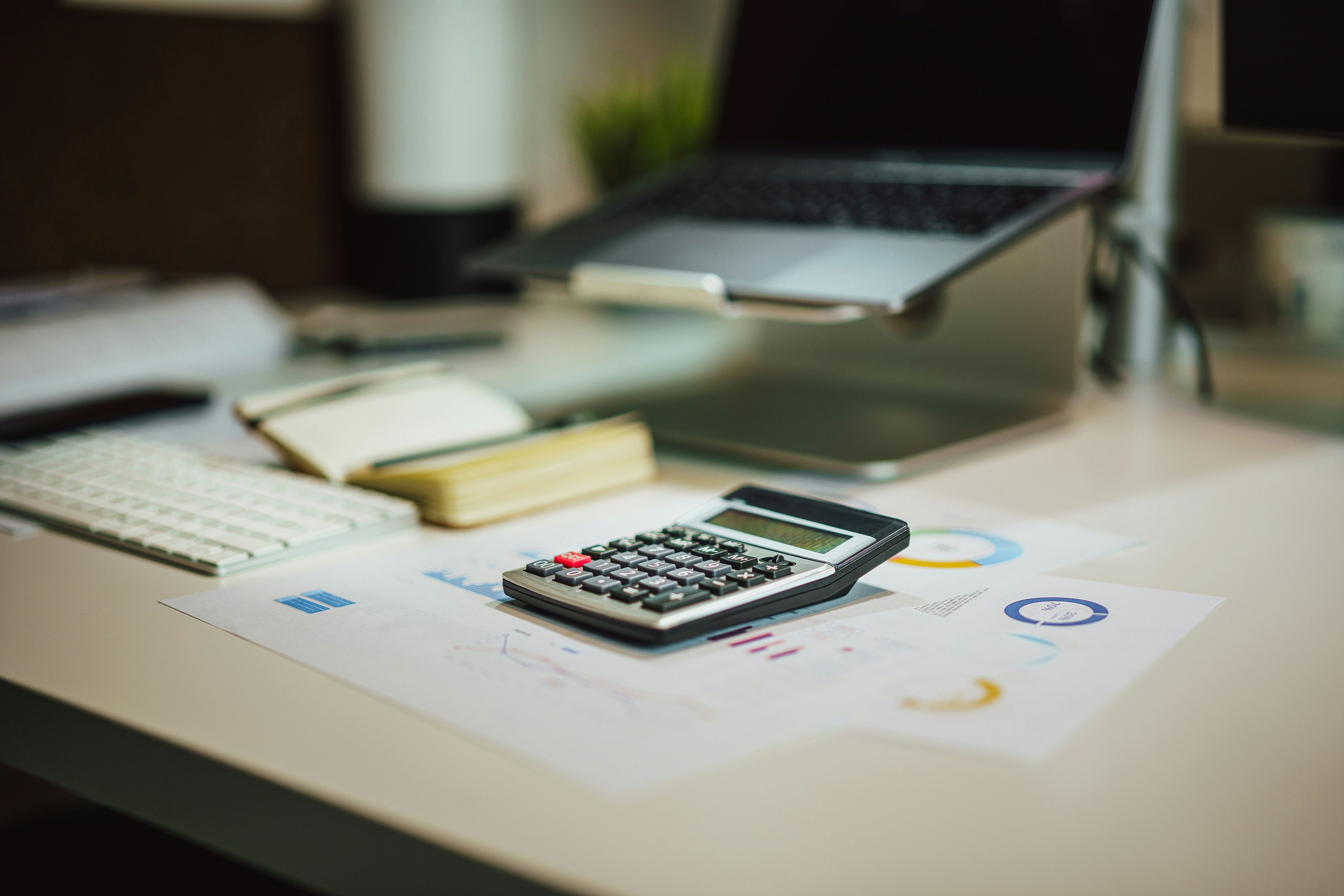 A calculator on a desk next to a laptop and notebook.