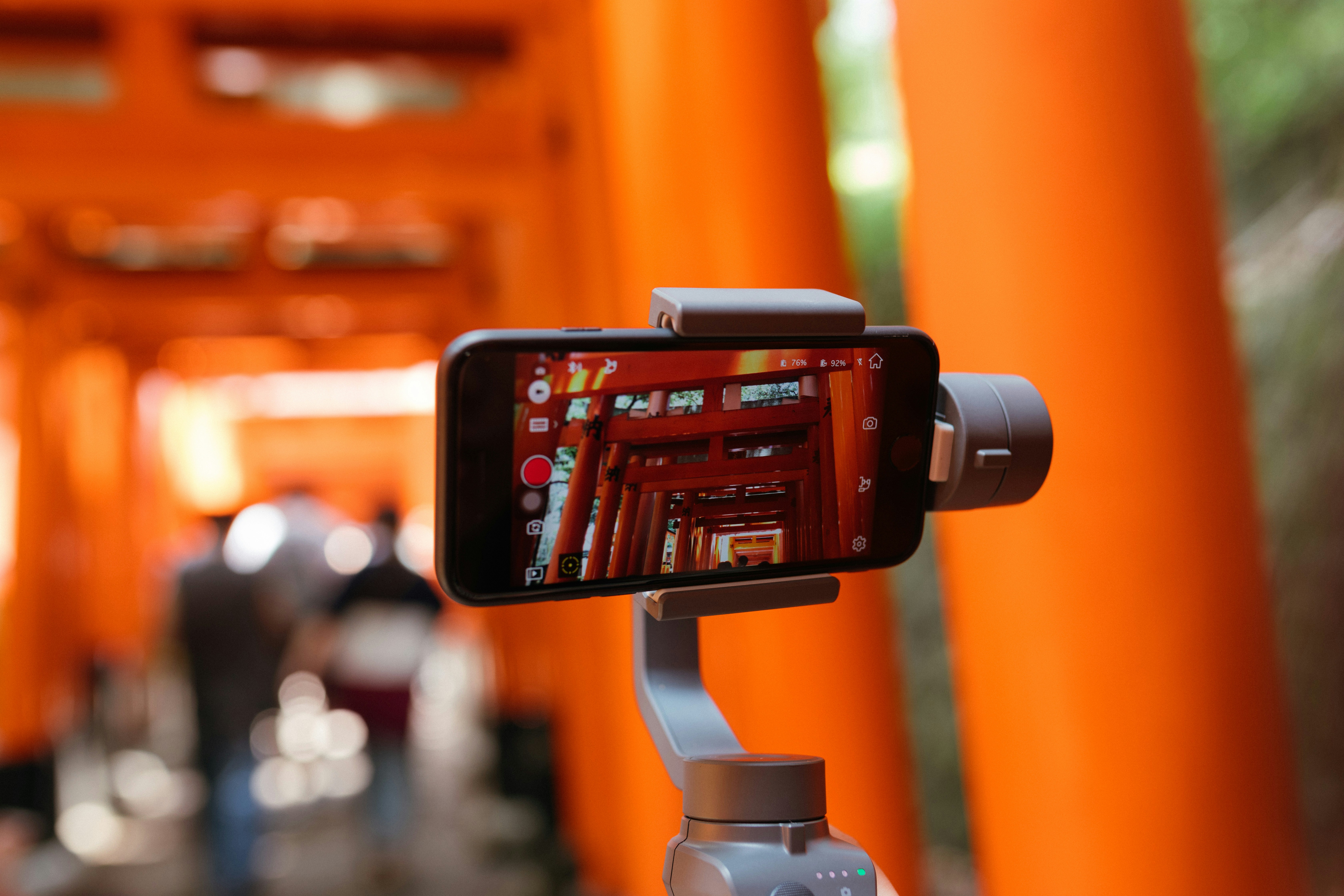 Smartphone on a gimbal stabilizer recording vertical video of an orange torii gate walkway.
