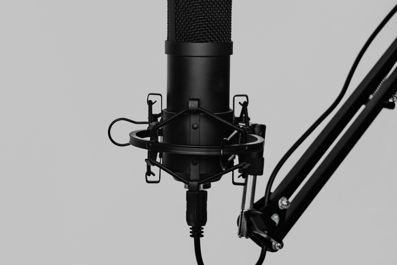 A black condenser microphone in a shock mount on an adjustable boom arm.