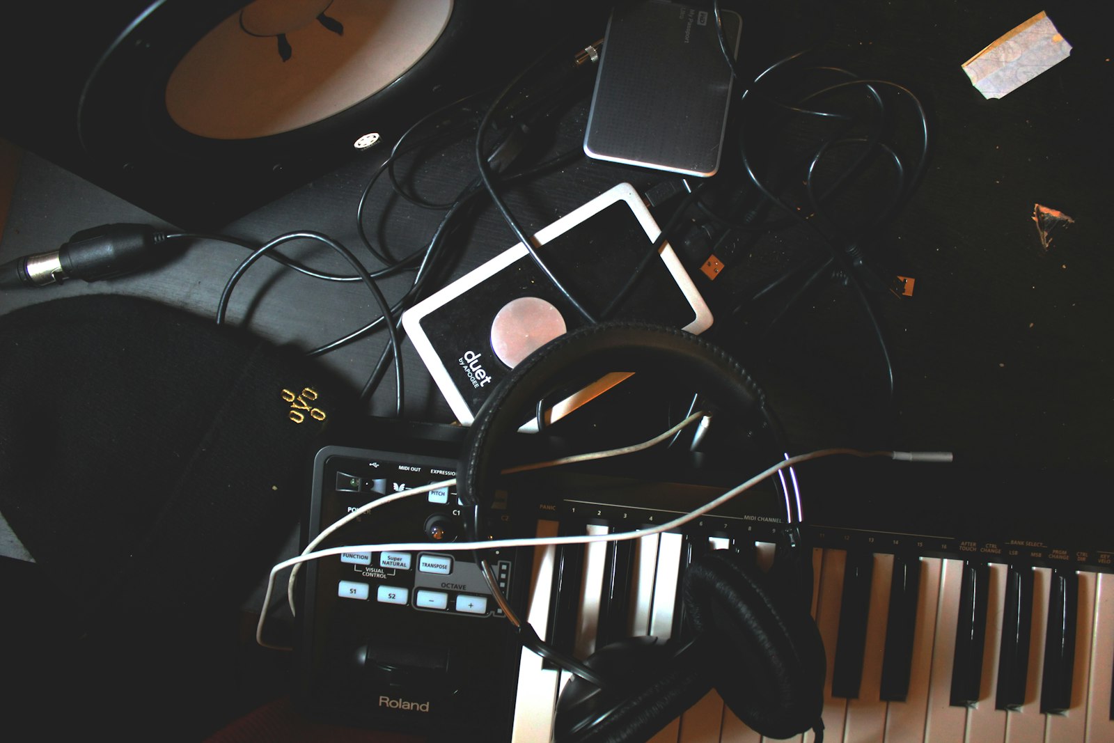 Flat-lay photo of headphones, a MIDI keyboard, and a speaker on a black surface.